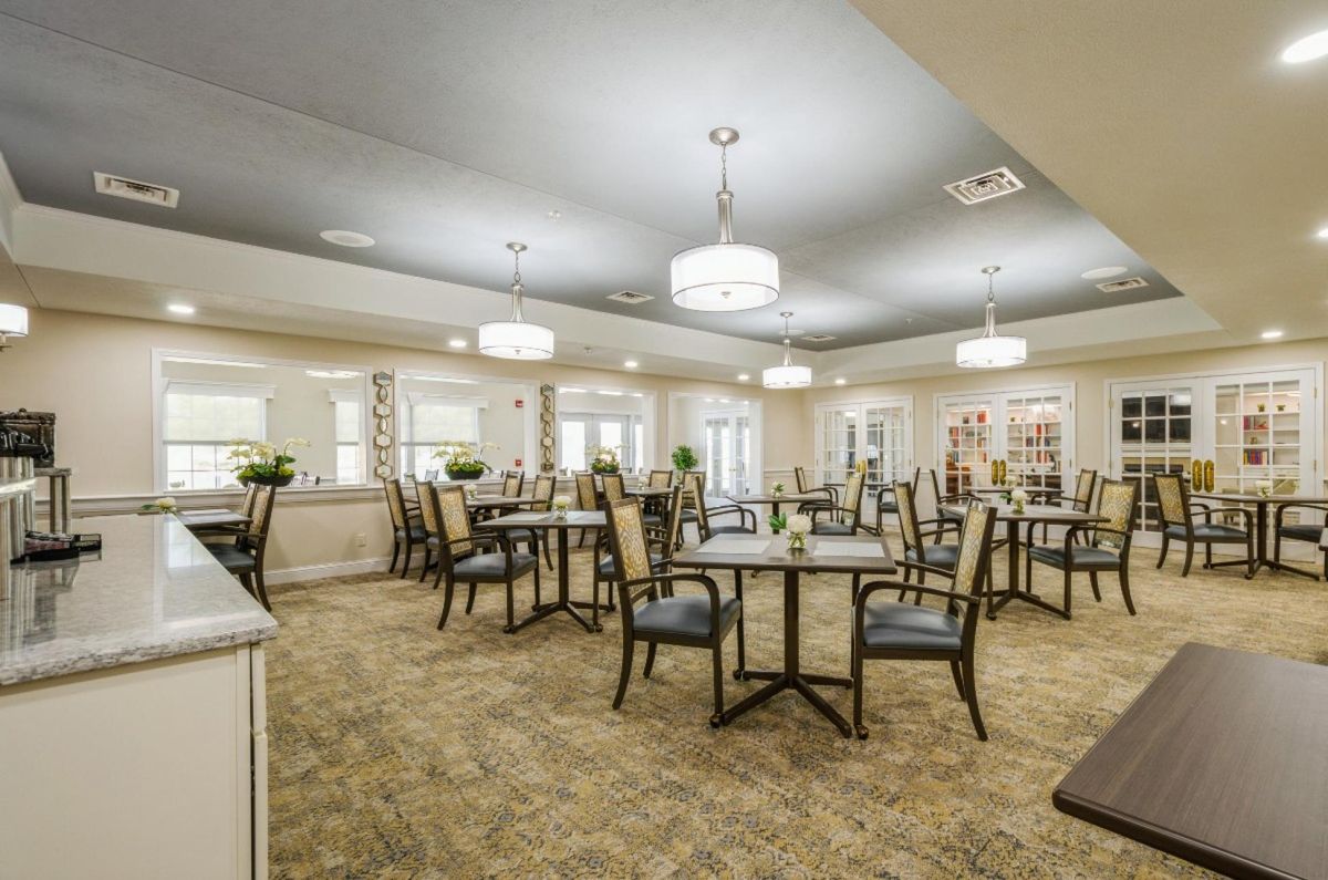 A spacious dining room with neatly arranged tables and chairs, featuring contemporary lighting fixtures and carpeted flooring.
