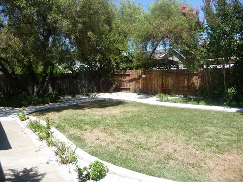 A well-maintained backyard with a lawn, trees, and a wooden fence.