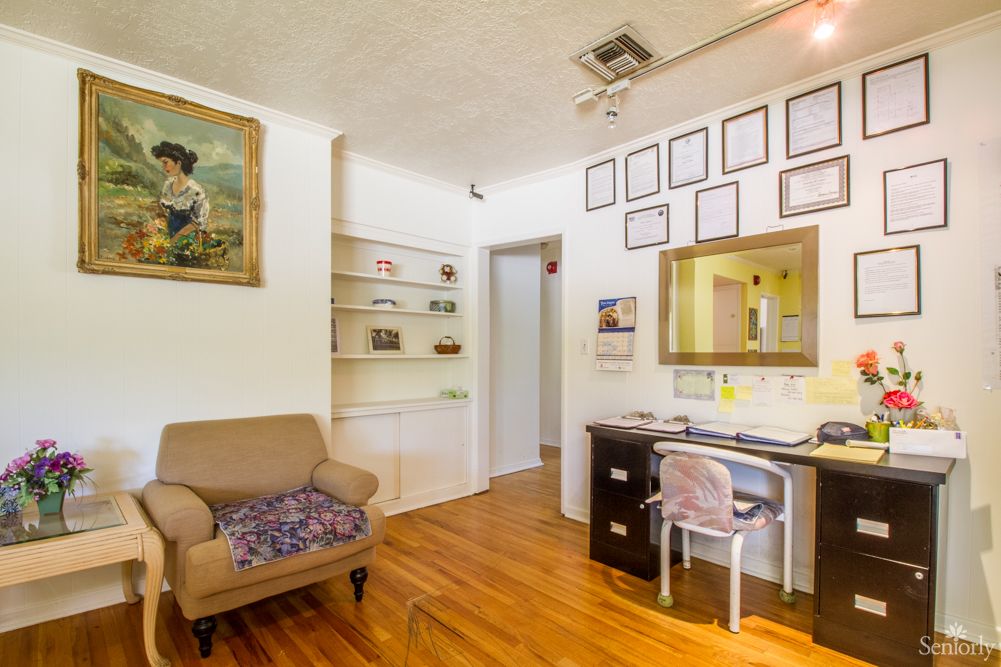 A cozy living room with an office space featuring a desk and chair, decorated with artwork and framed pictures.