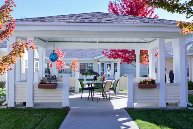 A cozy outdoor gazebo with seating, surrounded by autumn foliage.