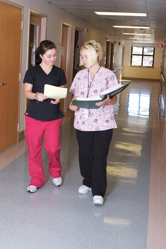 Two nurses discussing patient information while walking down a hospital hallway.