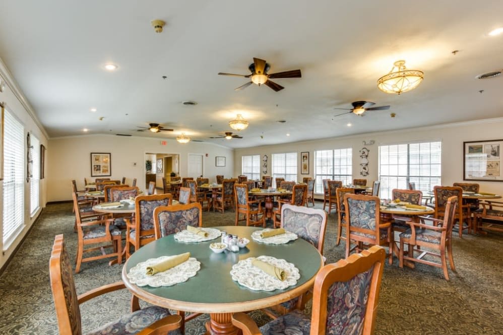 A spacious dining room with neatly arranged tables and chairs, featuring ceiling fans and ample lighting.