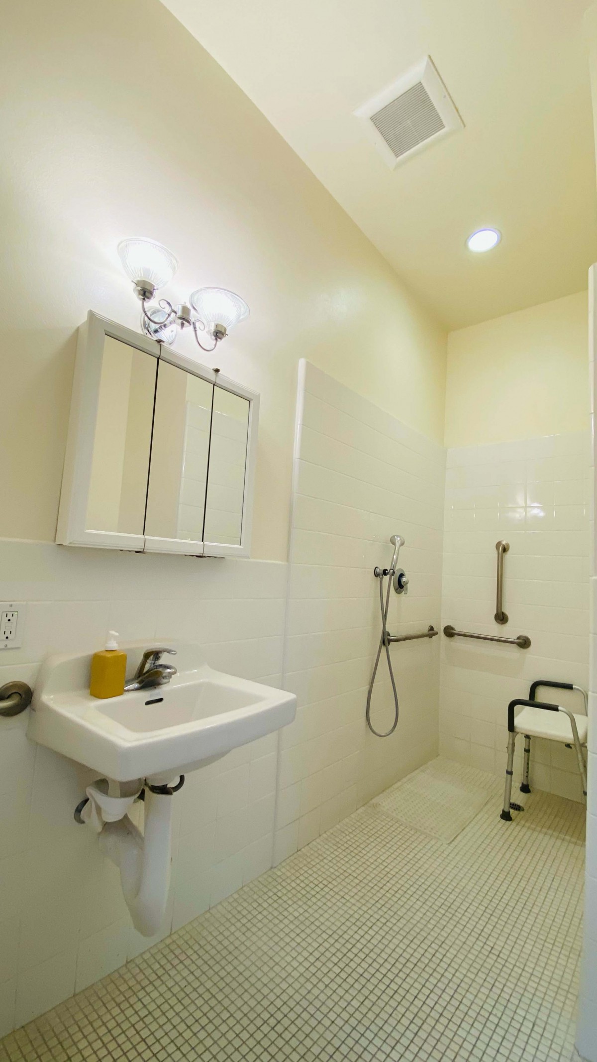 An accessible bathroom with a walk-in shower, grab bars, and a shower chair.