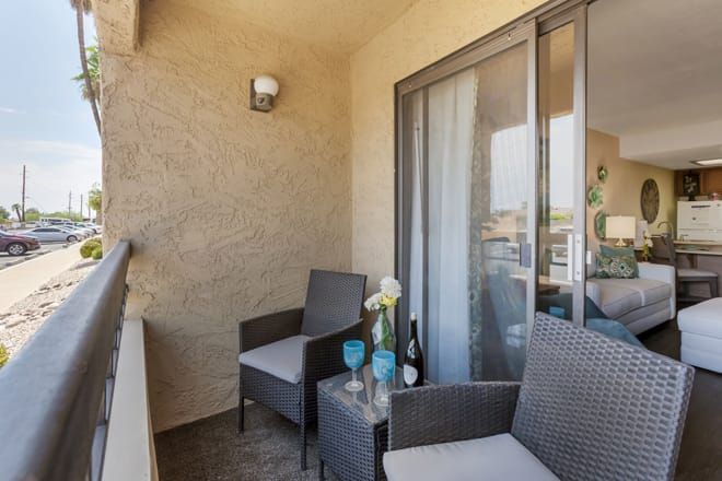 A cozy balcony with two chairs, a small table with wine and glasses, and a decorative vase of flowers.