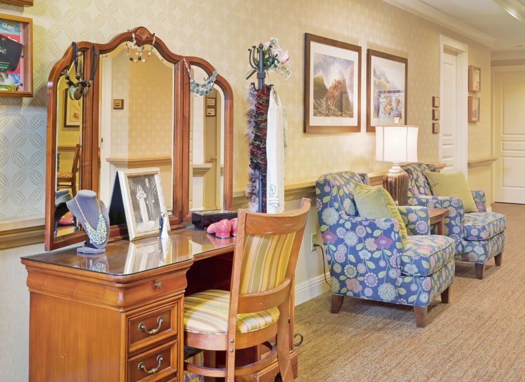 A cozy living room interior with a wooden vanity, upholstered chairs, and decorative artwork.