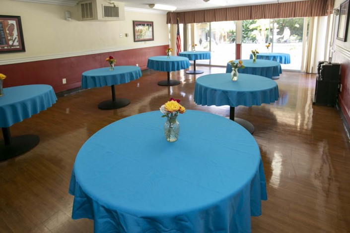 A banquet hall with round tables covered in blue tablecloths, each adorned with a vase of flowers.