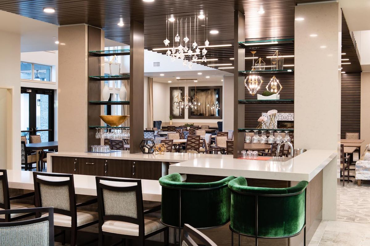 A modern and luxurious kitchen interior featuring elegant lighting, comfortable bar stools, and a sleek countertop.