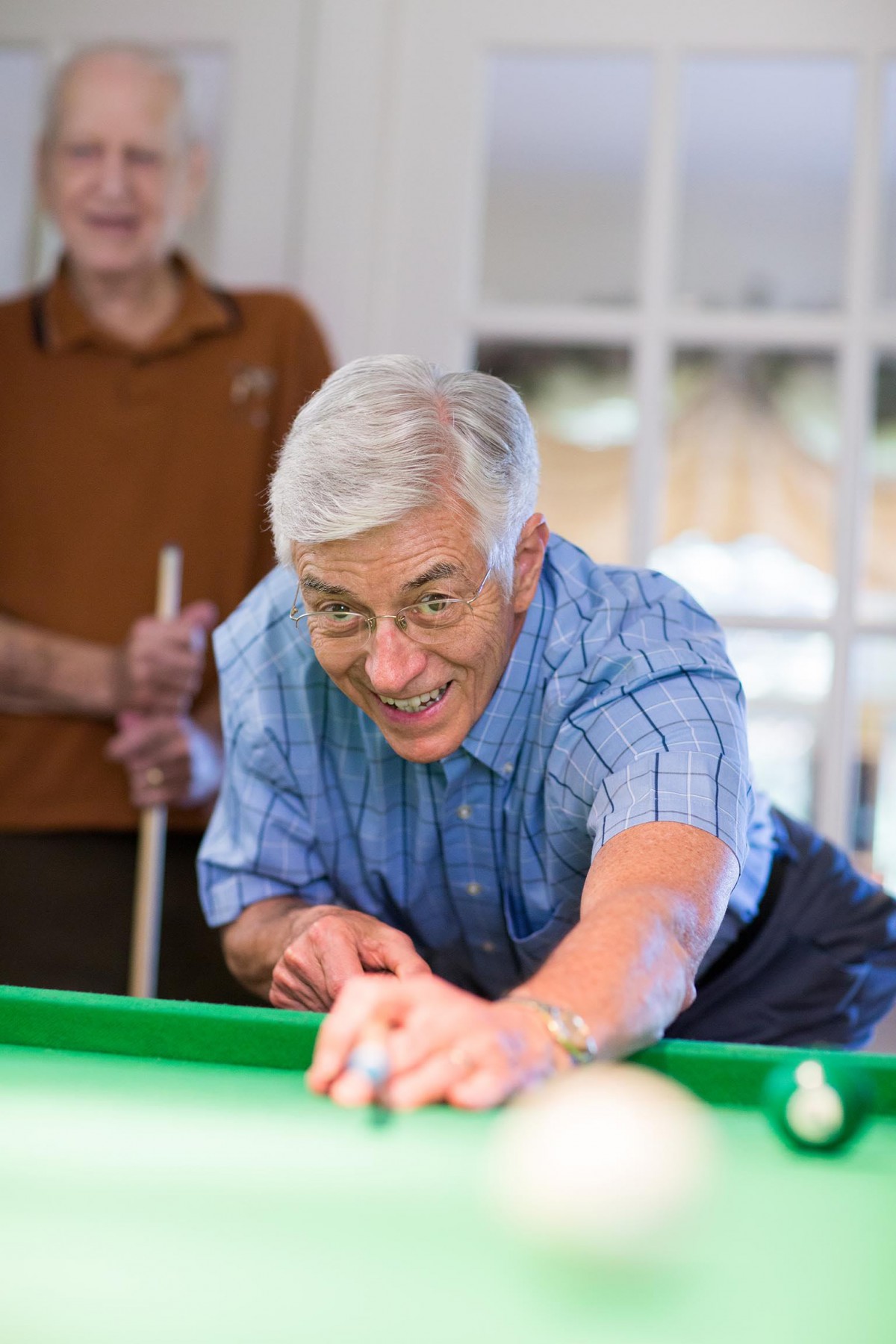 A senior man focuses intently as he takes a shot in a game of billiards.