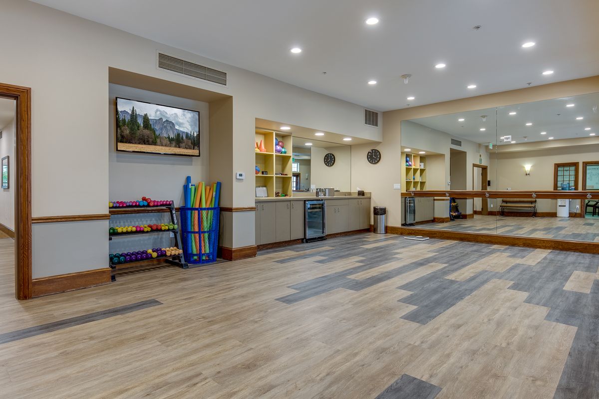 A spacious and well-lit exercise room with wooden flooring, mirrors, and various fitness equipment.