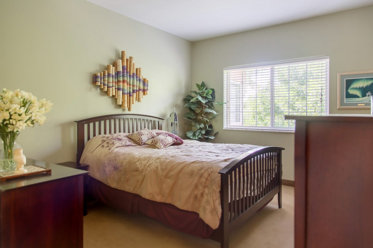 A cozy bedroom with a wooden bed, decorative wall art, and a large window.