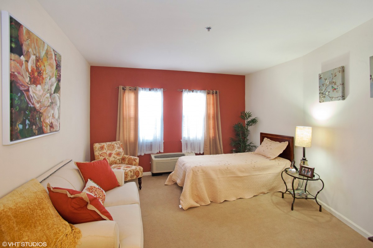 A cozy bedroom with a bed, sofa, and armchair against a warm-toned wall.