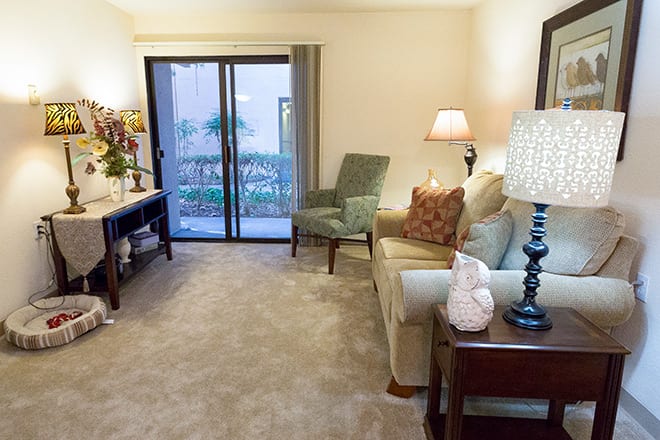 A cozy living room with a sofa, chairs, and a lamp beside a sliding door.