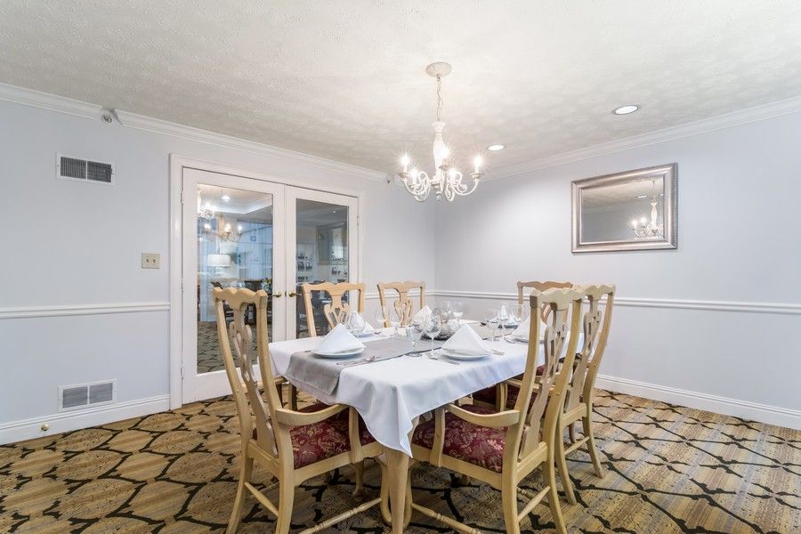 A well-lit dining room featuring a chandelier, a dining table with six chairs, and decorative elements like a mirror and patterned carpet.