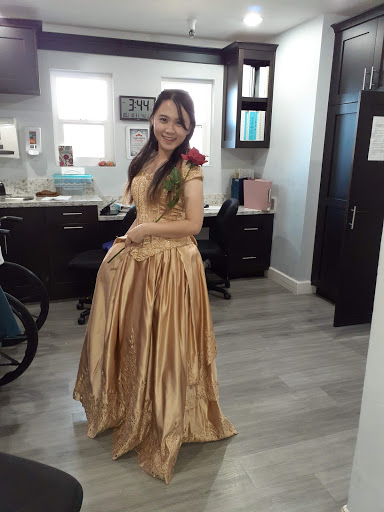 A radiant young woman poses gracefully in a stunning gold dress, complemented by a rose and an elegant smile.