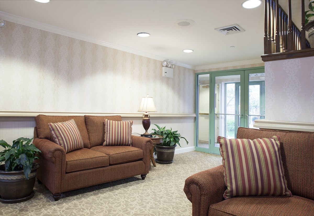 A cozy living room with brown sofas and striped cushions, featuring a lamp and a potted plant.