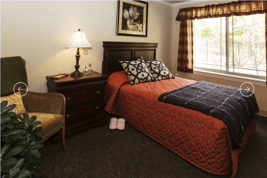 A cozy bedroom with a neatly made bed, nightstand, and a warm lamp.