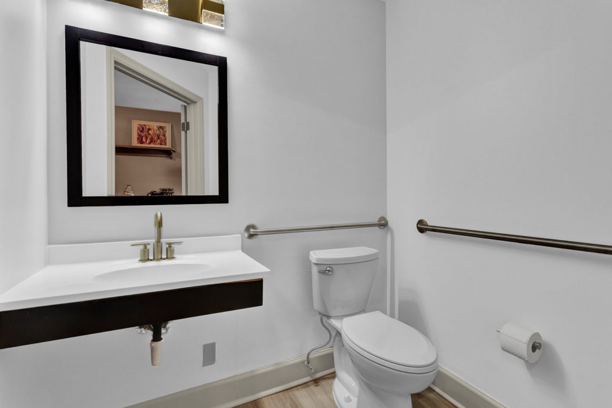 A modern bathroom with a toilet, sink, and grab bars.