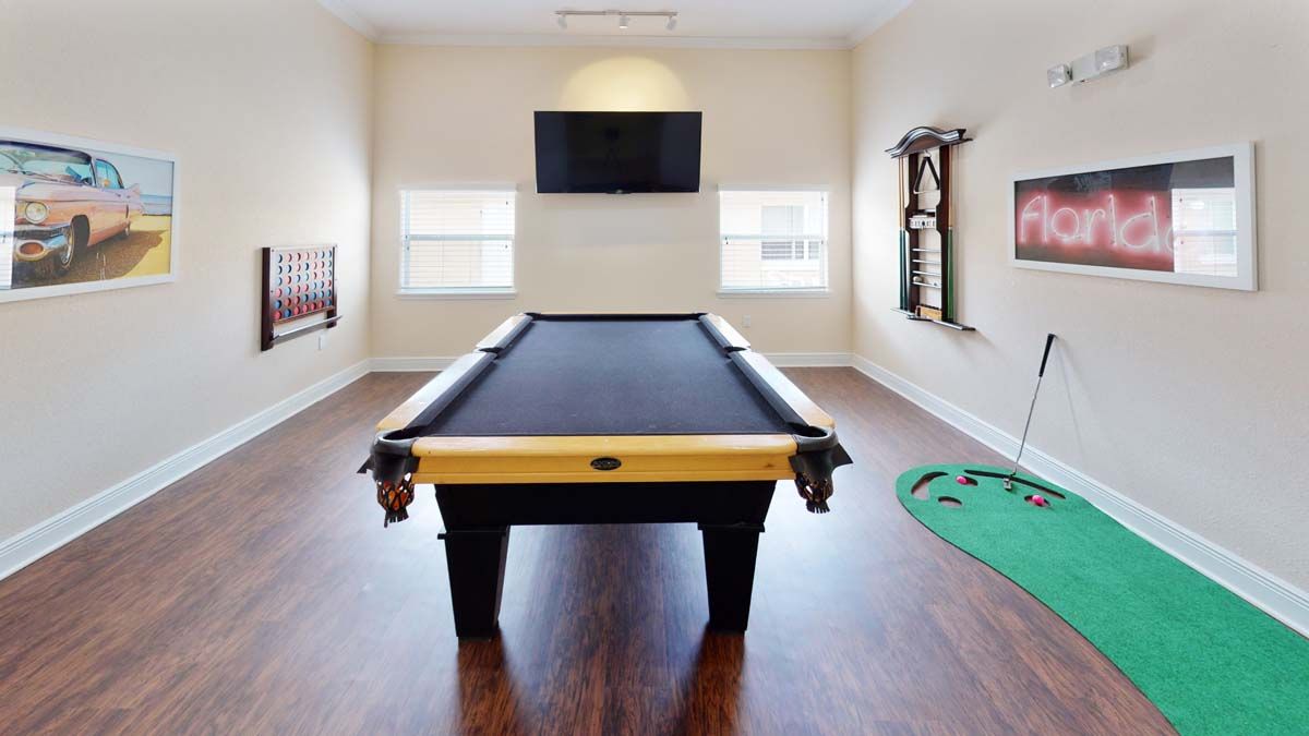 A well-lit game room featuring a billiard table, television, and wooden flooring.