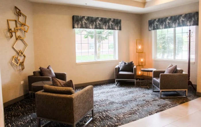 A cozy living room with modern chairs, a decorative carpet, and large windows.