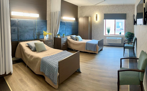 A modern, well-lit hospital room featuring two beds with elegant furnishings and a calming color palette.