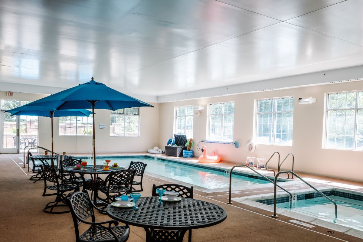 An indoor swimming pool with seating and an umbrella for relaxation.