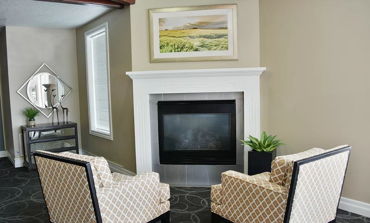 A cozy living room with two patterned armchairs facing a fireplace and a piece of artwork above it.