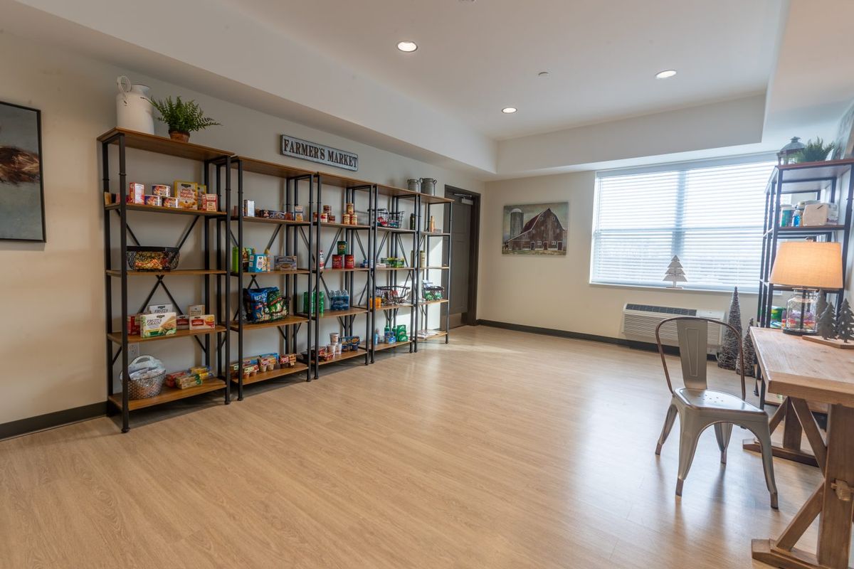 A spacious and well-lit room featuring wooden floors, decorative shelves, and a large window.