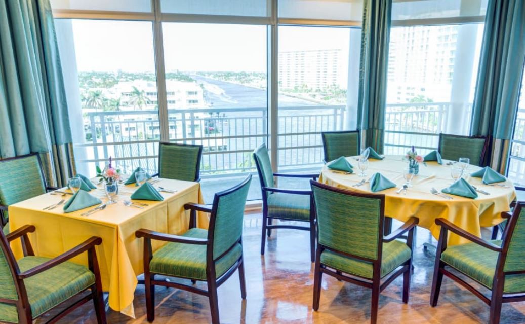 A well-set dining area with tables and chairs overlooking a scenic view through large windows.