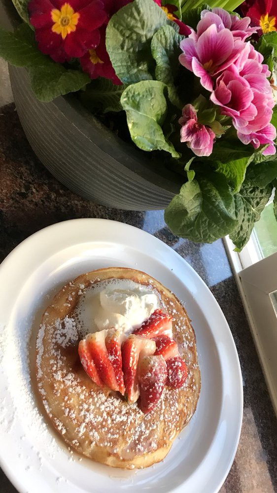 A delicious pancake topped with strawberries, cream, and powdered sugar next to a flower pot.