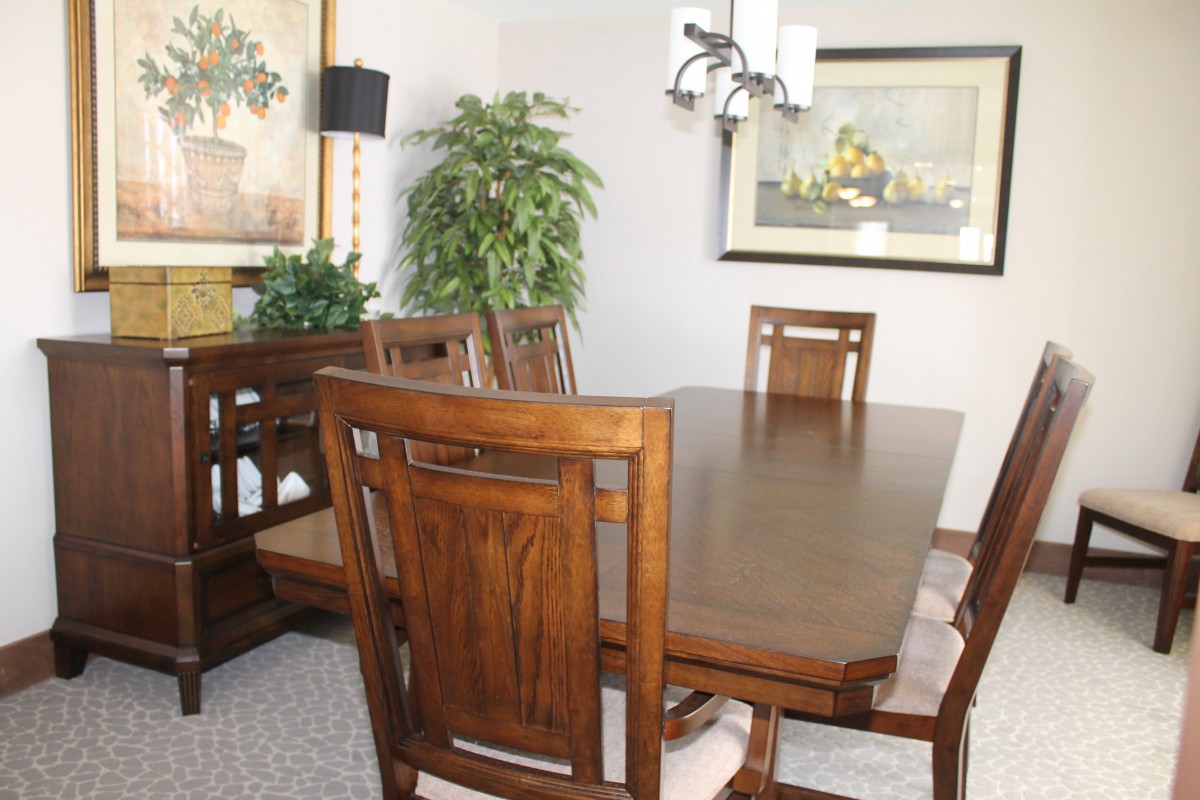 A well-furnished dining room featuring a wooden table and chairs, with decorative plants and artwork.