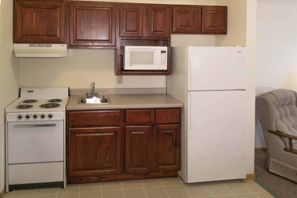 A simple kitchen with wooden cabinets, a microwave, refrigerator, stove, and a sink.
