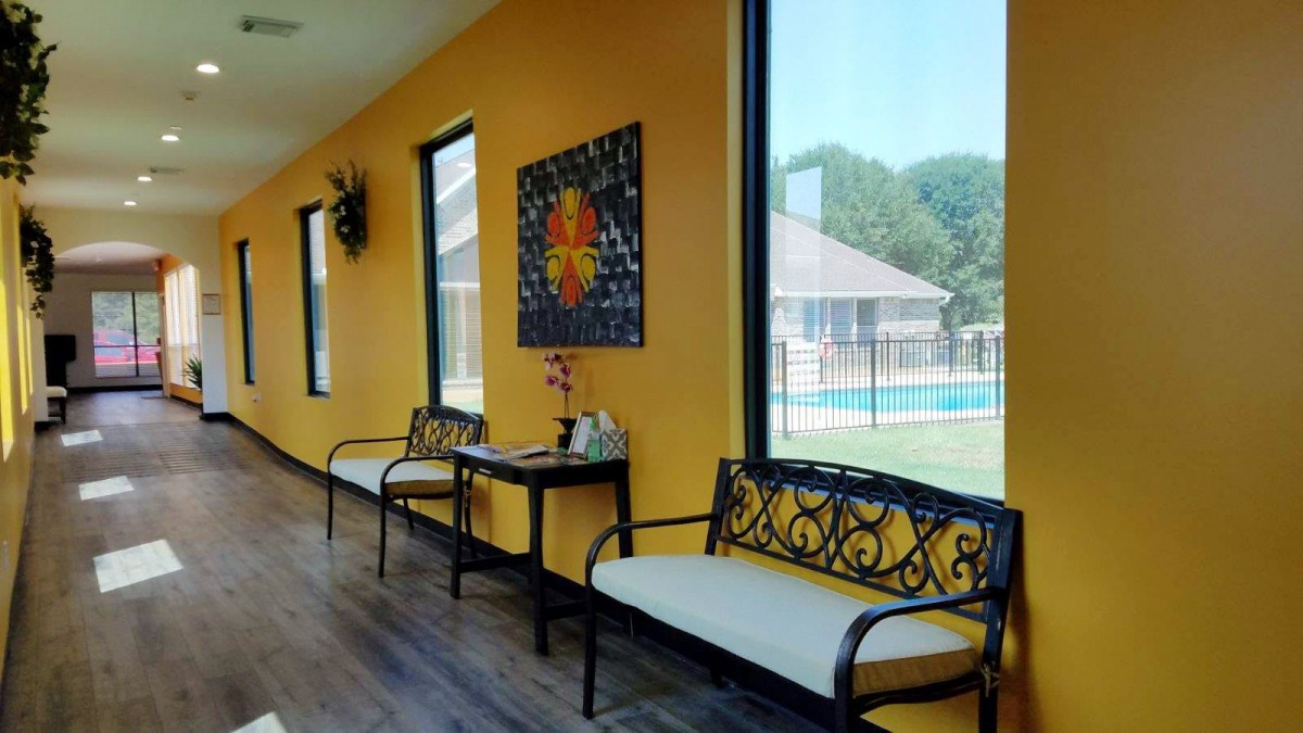 A modern interior waiting area featuring ornate benches, large windows, and bright yellow walls.