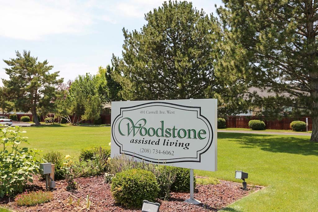 A sign for Woodstone Assisted Living surrounded by a well-maintained lawn and trees.