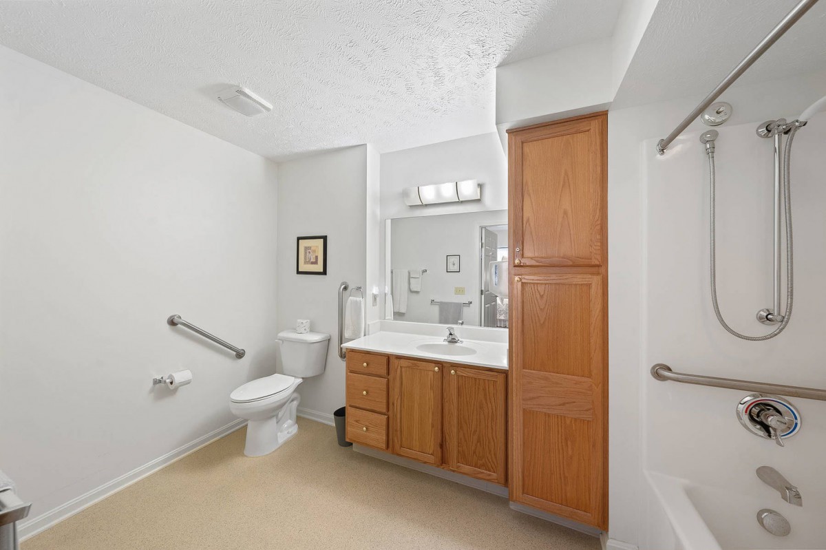 A clean bathroom with wooden cabinets, a toilet, and a large mirror above the sink.