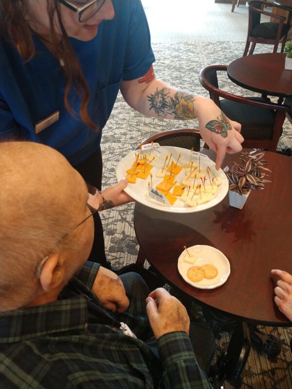 A person with tattoos serves a plate of snacks to someone sitting at a table.