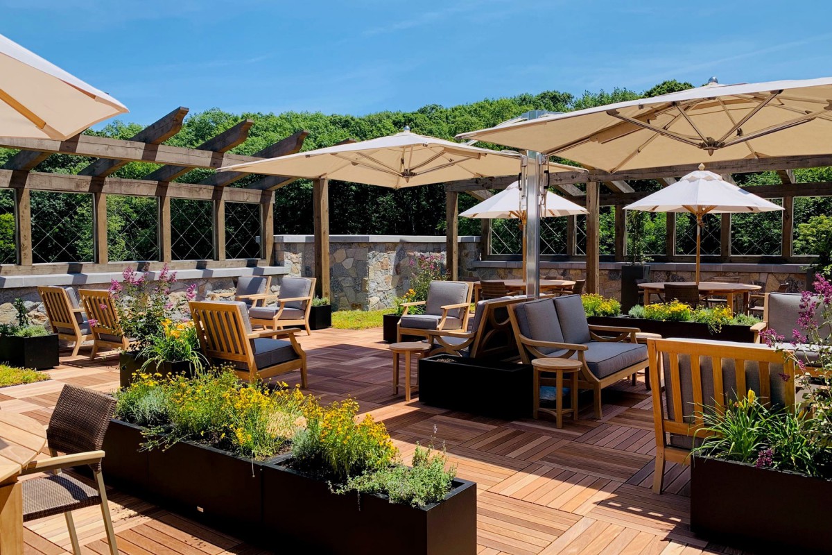 An inviting outdoor patio with comfortable seating, umbrellas, and lush greenery on a sunny day.