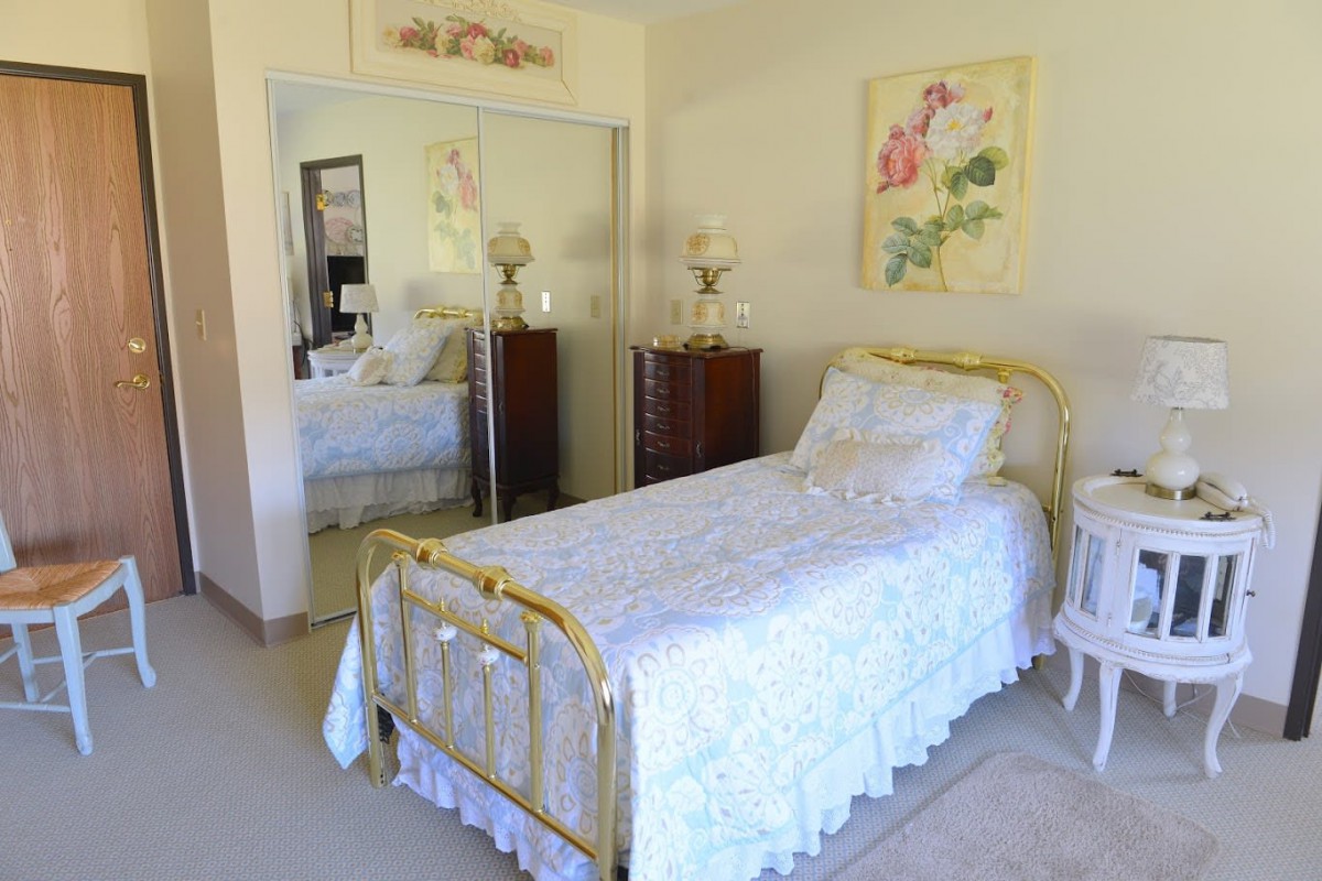 A cozy bedroom featuring a single brass-framed bed with floral bedding, mirrored closet doors, and elegant decor.