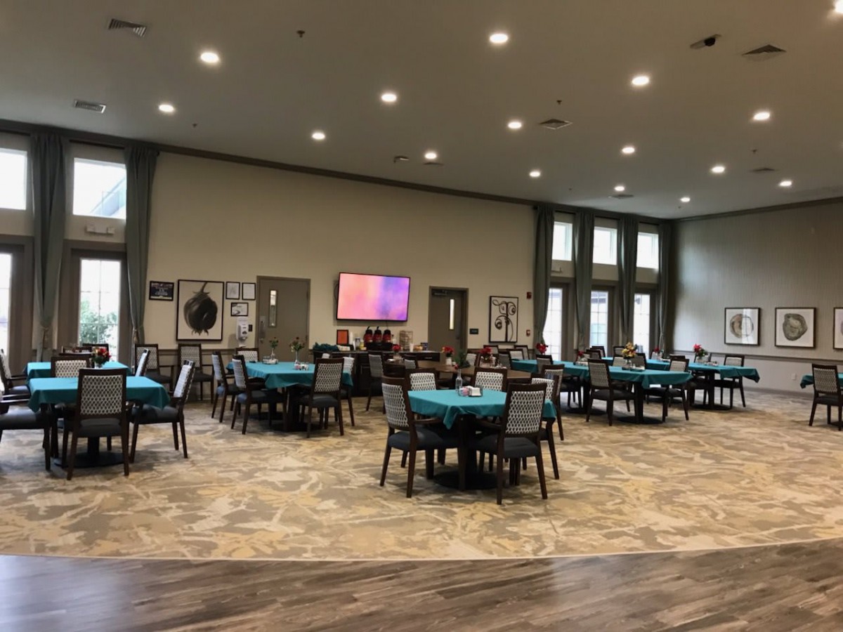 A spacious event hall with round tables covered in teal cloths, neatly arranged for an upcoming gathering.