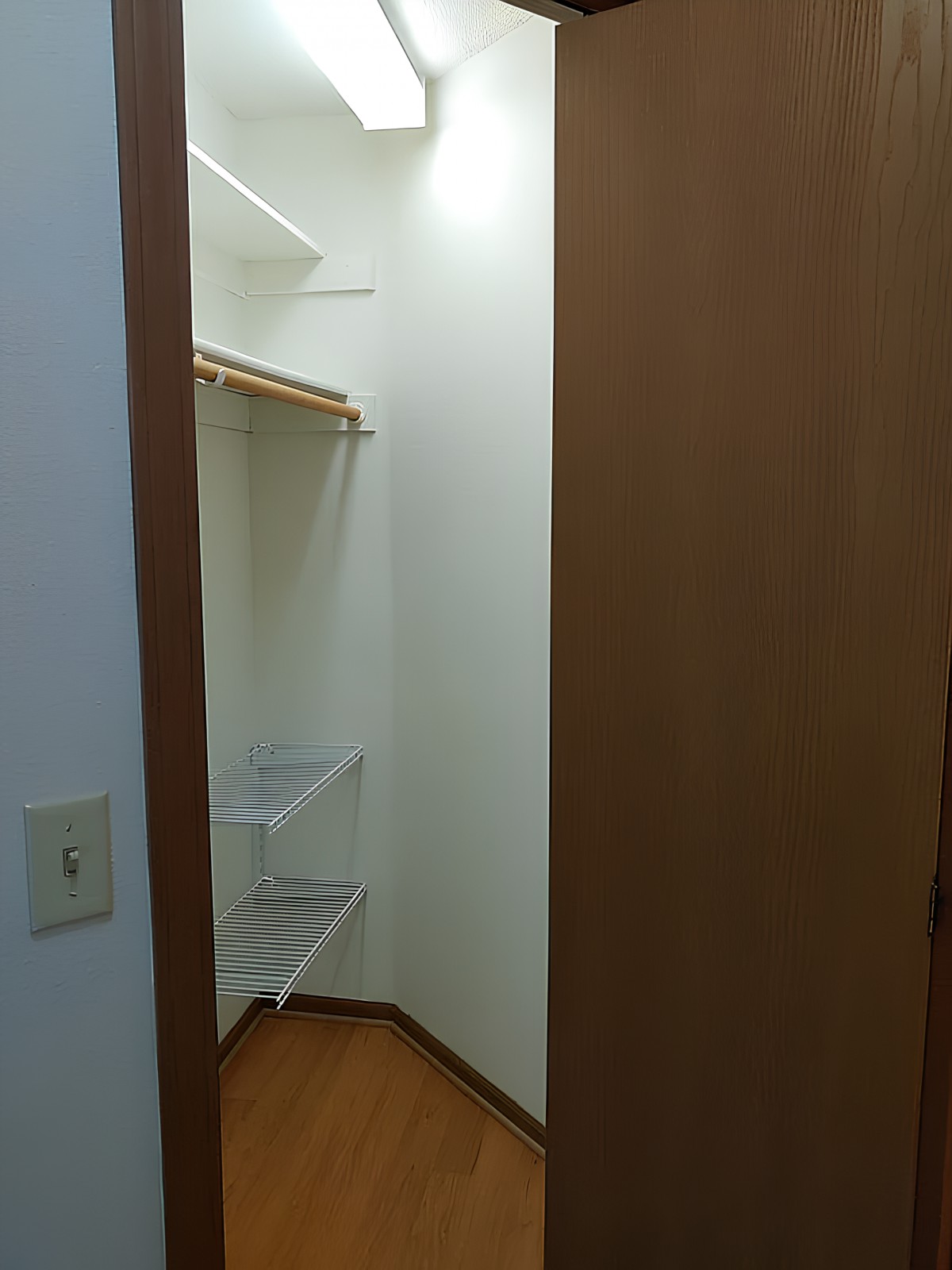 An empty closet with wooden shelves and an open wooden door.