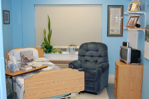 A cozy office space featuring a blue recliner chair, a desk cluttered with papers, and a green plant by the window.