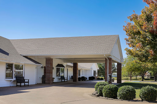 A welcoming entrance to a residential building surrounded by well-maintained landscaping under a clear blue sky.