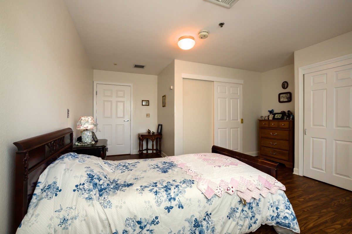 A cozy bedroom with floral bedding, a wooden dresser, and warm lighting.