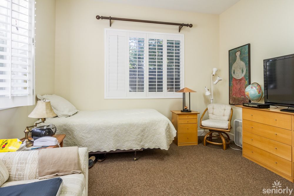 A cozy bedroom featuring a single bed, chair, and a painting on the wall.