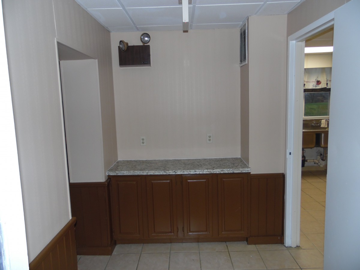 An empty room with a countertop and cabinetry under fluorescent lighting.
