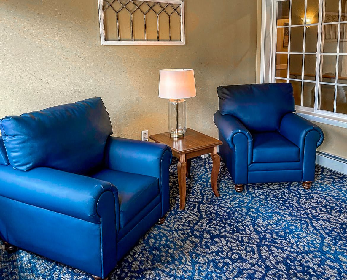 A cozy living room with two blue armchairs, a wooden coffee table, and a patterned carpet.