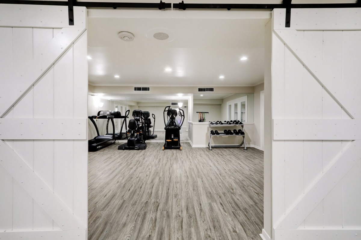A modern home gym with various exercise equipment, including treadmills and weights, in a spacious room.