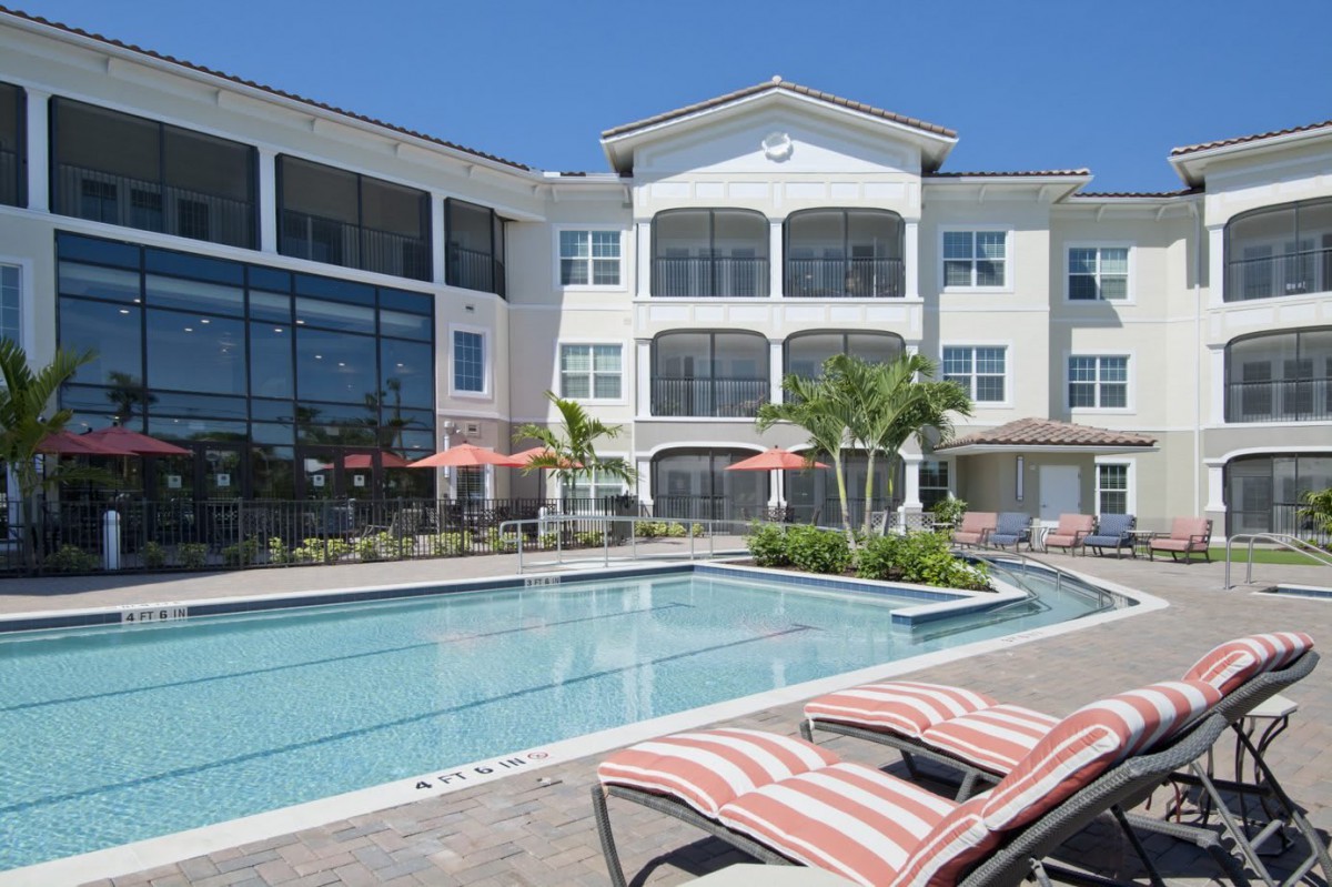 A sunny day at a modern apartment complex with a pool and palm trees.