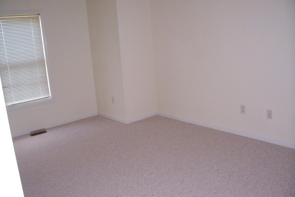 An empty room with carpeted flooring and plain walls.