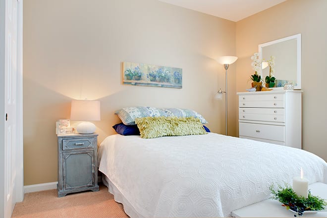 A cozy bedroom with a neatly made bed, featuring a bedside table and a floor lamp.