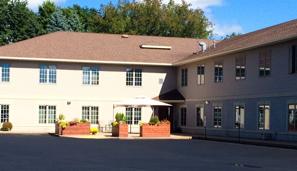 A sunny exterior view of a residential building with plants and an entrance area.